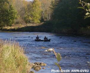 Canoers paddles down a river in a natural area.